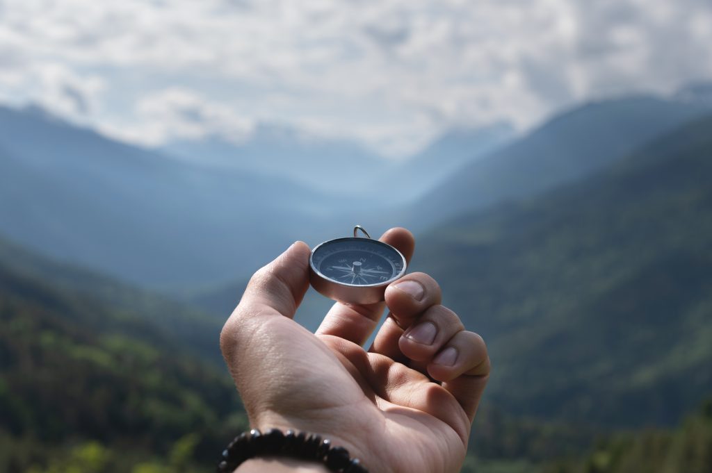 a hand holding a compass in front of a mountain range - New Jersey Court-Mandated Mediation